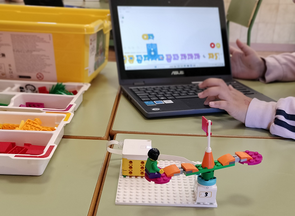 Mesa con piezas LEGO y un modelo conectado a un ordenador portátil que muestra un programa de bloques para robótica educativa.